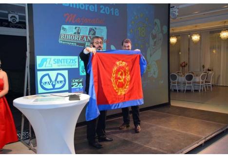 CU DOUĂ FEŢE. În lipsă, europarlamentarul Emilian Pavel a primit cadou un steag cu două feţe: pe-o parte este cel al Uniunii Europene, de unde PSD-istul îşi ia salariul de multe mii de euro, iar de cealaltă parte drapelul Partidului Comunist Român, care pare să-i ghideze pe social-democraţi în activitatea din ţară