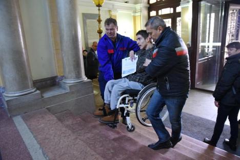 Umilitor! Orădeni cu dizabilităţi locomotorii, căraţi pe braţe de angajaţii Primăriei, ca să depună o petiţie (FOTO / VIDEO)